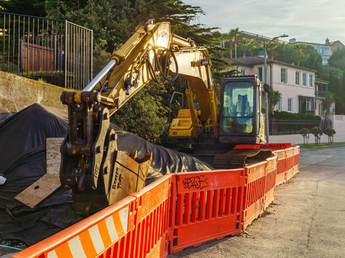 Excavator at an urban construction site behind safety barriers
