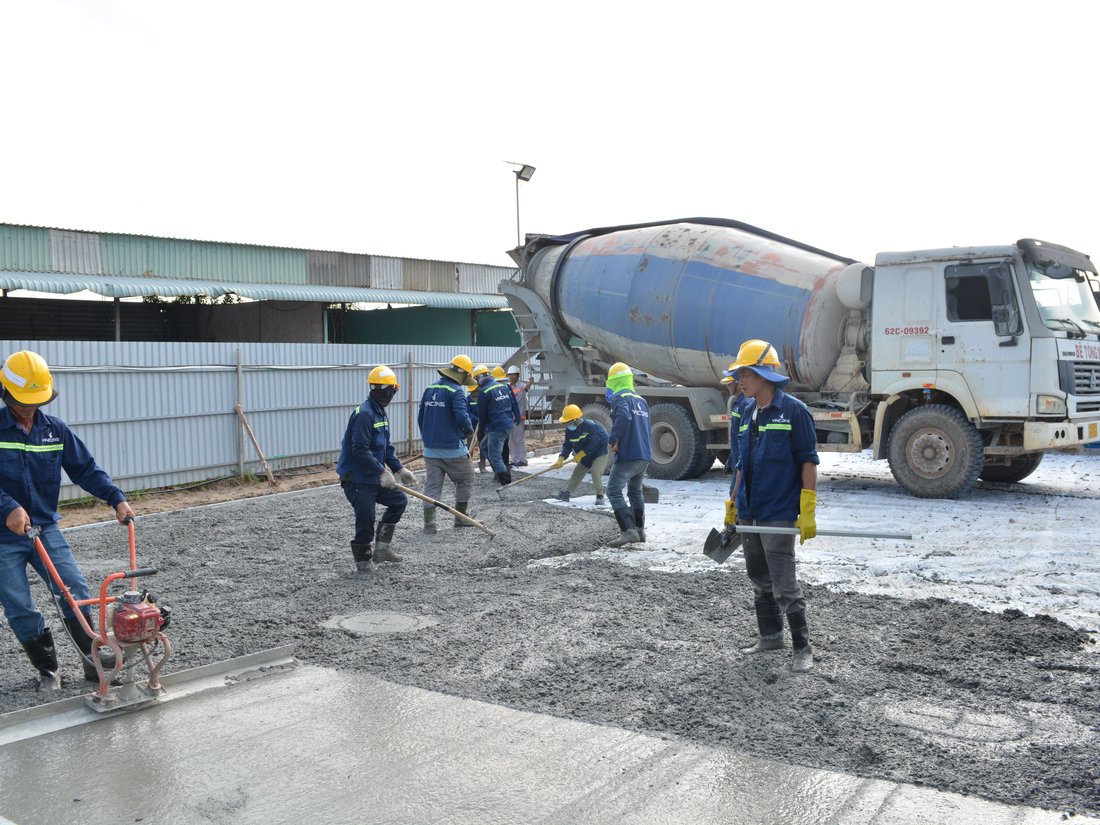 Crew finishing a freshly poured concrete slab with a mixer truck behind