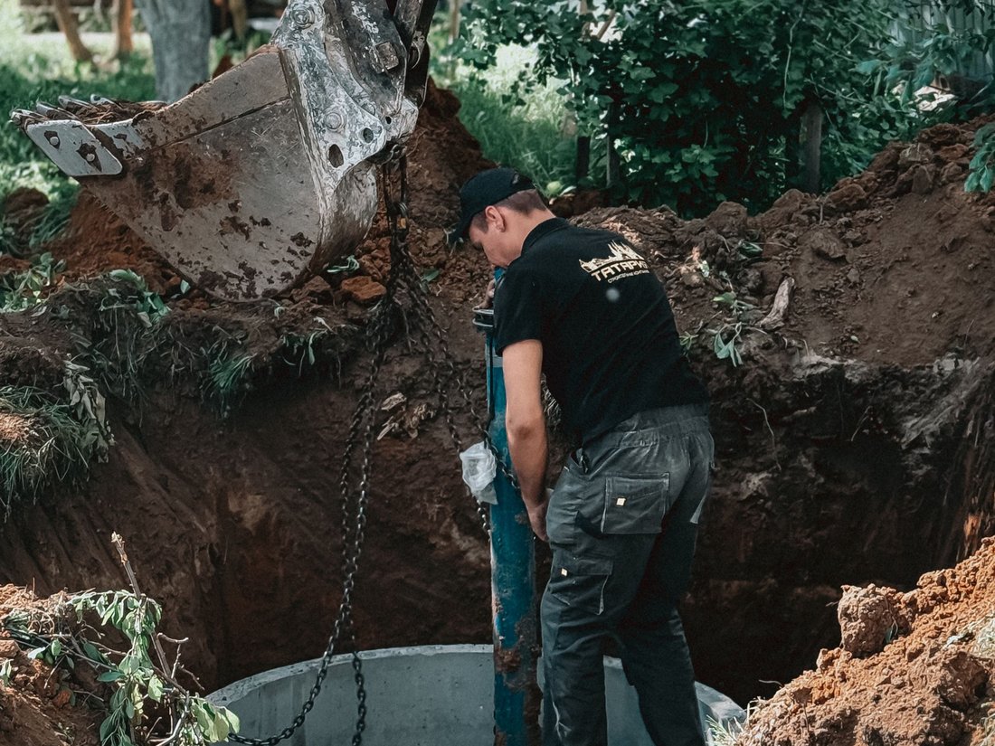 Worker installing a precast concrete manhole structure in an excavation